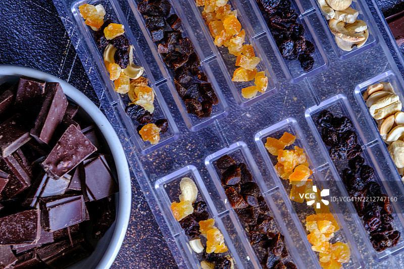 俯视图：巧克力制作过程，配有坚果、干果和紫色花朵，背景为石材。图片素材