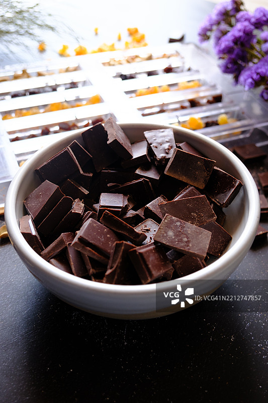 俯视图：巧克力制作过程，配有坚果、干果和紫色花朵，背景为石材。图片素材