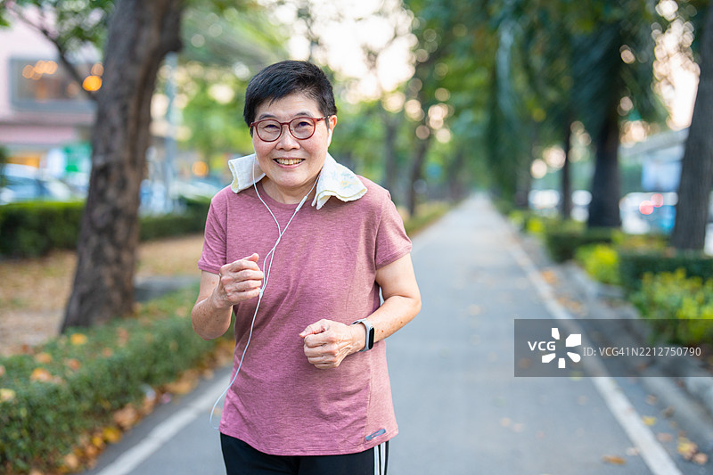 一位老年女性戴着耳机走路锻炼。图片素材