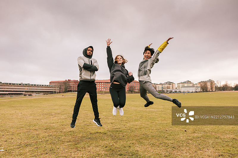 三位朋友穿着运动服在公园里一起跳跃，散发着积极的能量。图片素材