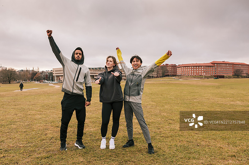 三位朋友穿着运动服在公园里合影，散发着积极的能量。图片素材