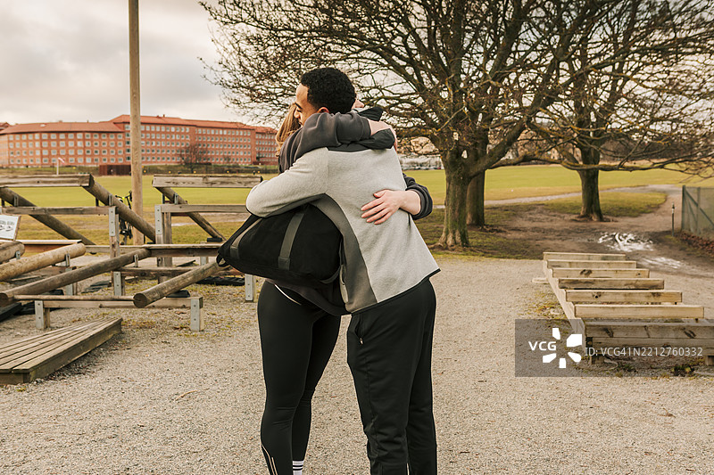 一对年轻情侣穿着运动服在户外健身房相拥而遇。图片素材