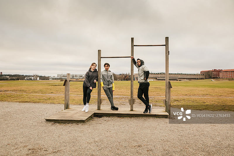 三位朋友在户外健身房一起合影。图片素材