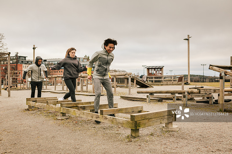 三个朋友在户外健身房互相鼓励做跳跃运动。图片素材