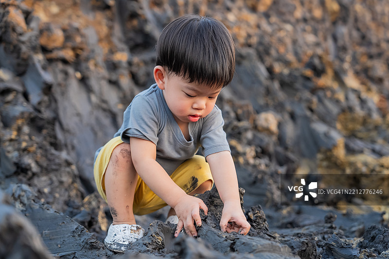 探索亚洲幼儿在户外泥土山坡上玩耍的快乐时光，男孩学习探索新的自然体验。图片素材