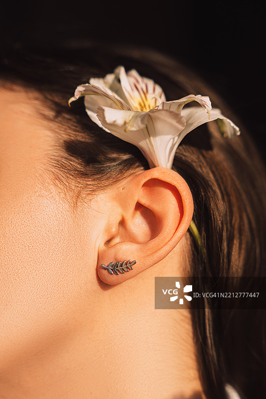 美丽女性耳朵特写，耳边有花和耳环，腮腺瘘，耳朵瘘管的罕见现象图片素材