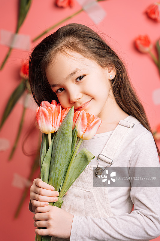 一位哈萨克混血女孩的肖像，背景是粉色的美丽郁金香，作为母亲节的惊喜。图片素材