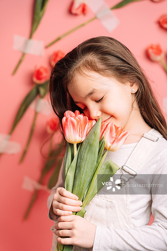 长发棕色头发的孩子在粉色背景上闻一束郁金香，母亲节图片素材