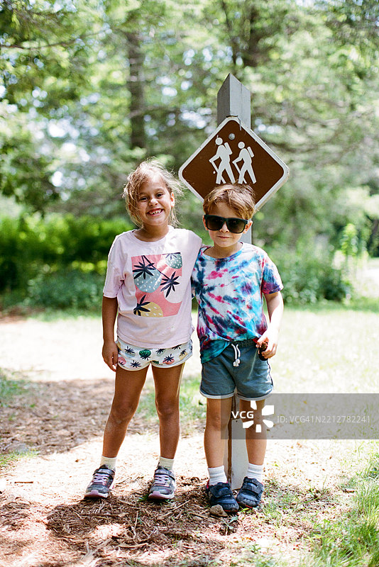 两个小学生，面带微笑，准备徒步，身后是徒步指示牌。图片素材