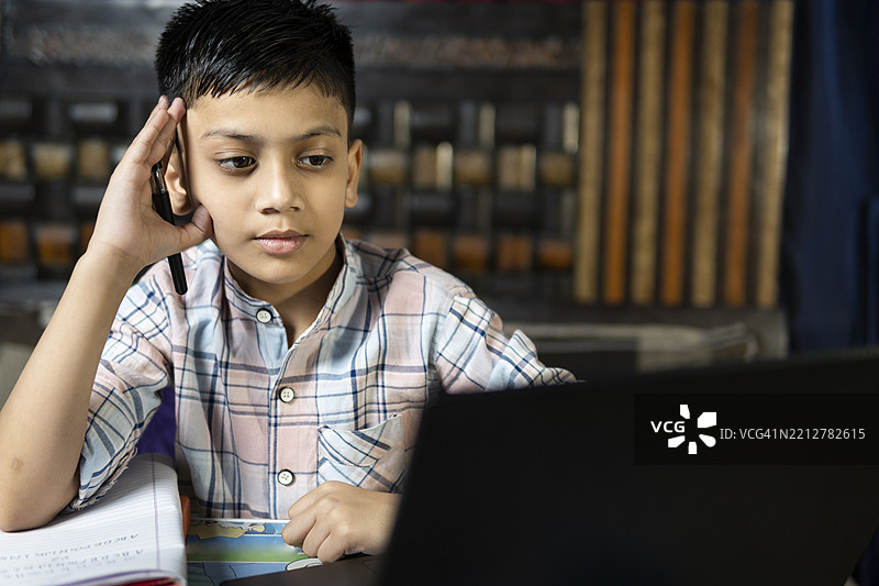 印度男孩在家用笔记本电脑学习，写笔记，做作业。图片素材