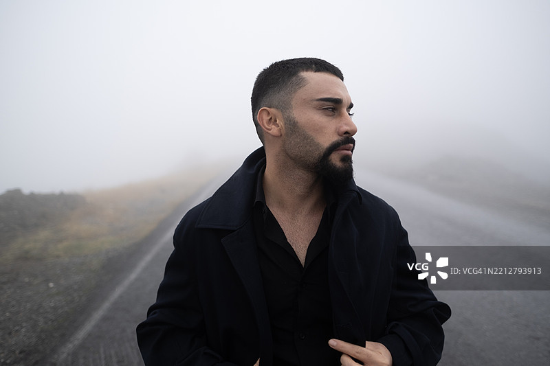 年轻男子在弥漫着忧郁雾气的道路上行走。图片素材