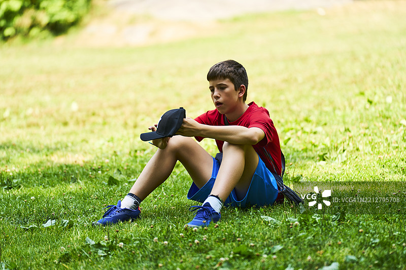 青少年运动员在草地上休息，手里拿着帽子，刚刚训练完。图片素材