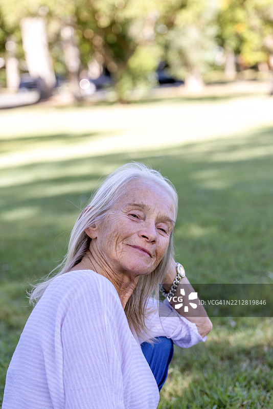 美丽快乐的老年女性坐在公园里，面带微笑地看着镜头，背景留有空白空间。图片素材