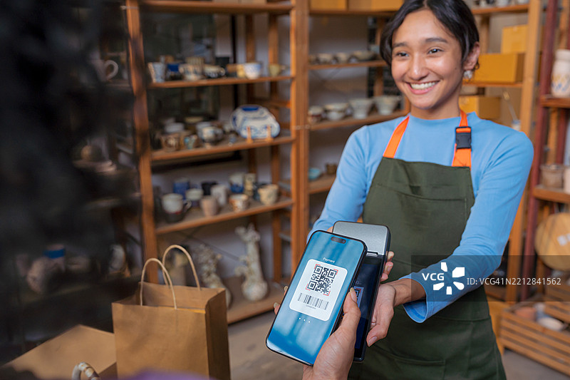 顾客在陶艺店用智能手机扫描二维码付款。图片素材