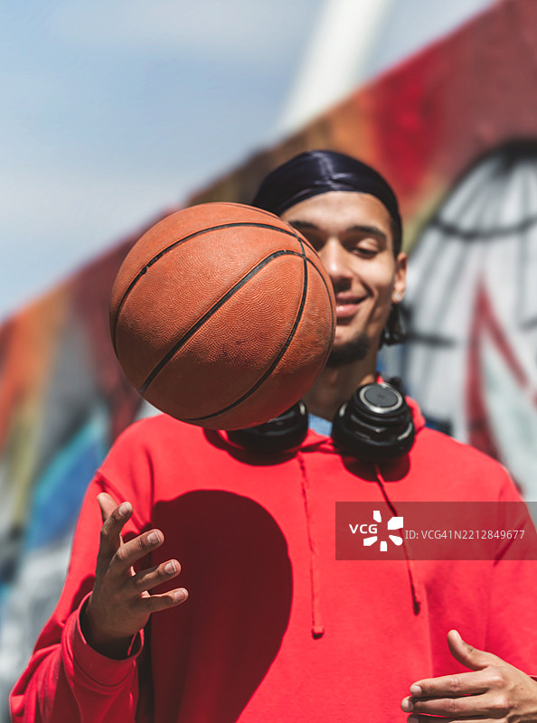 微笑的年轻运动员在户外的墙前平衡篮球图片素材