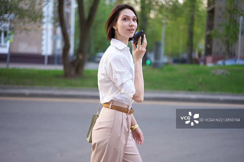 年轻女性在户外微笑着使用智能手机语音助手图片素材