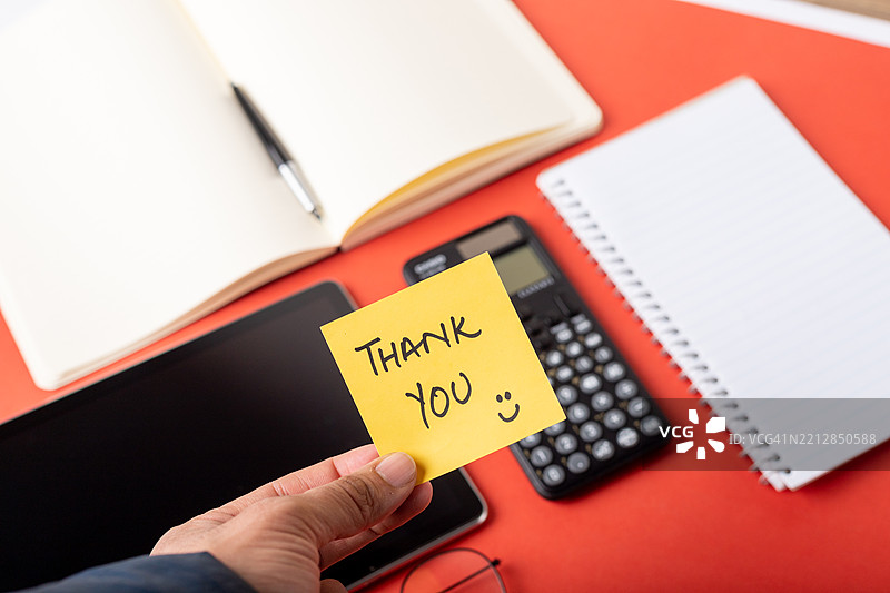 手握感谢卡在红色工作空间上图片素材