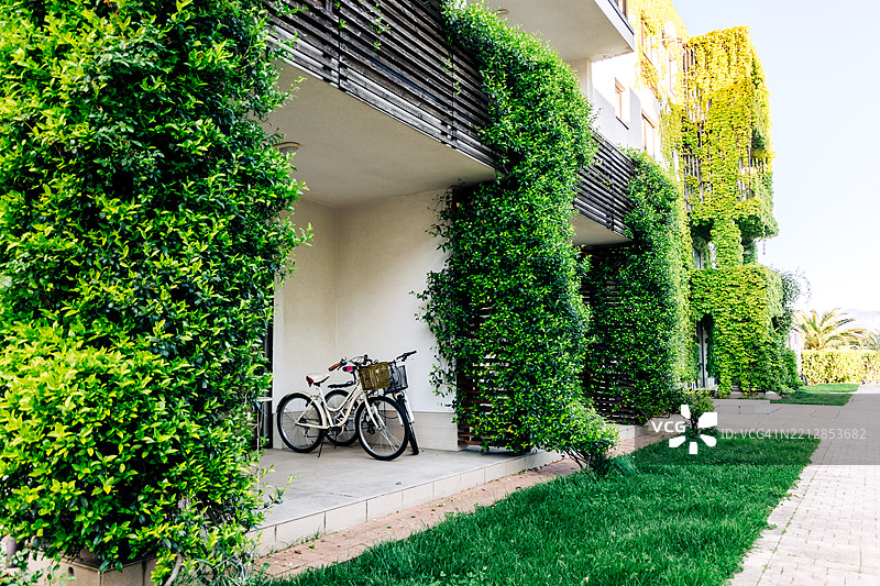被郁郁葱葱的植被覆盖的绿色住宅楼，旁边停放着自行车图片素材