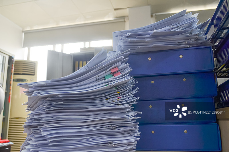 堆满待处理文件和文件箱的办公桌，工作压力概念。图片素材