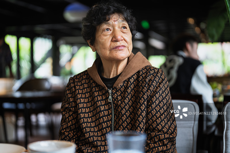 在温馨的餐厅里，沐浴在自然光中的沉思老年女性图片素材