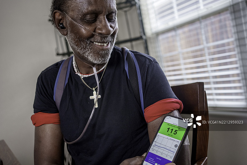 七十多岁的非裔美国老人用智能手机扫描他的连续血糖监测仪（CGM），以确保他的血糖处于健康范围。图片素材