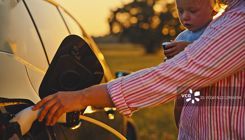 母亲在乡村环境中抱着小男孩为电动车充电图片素材