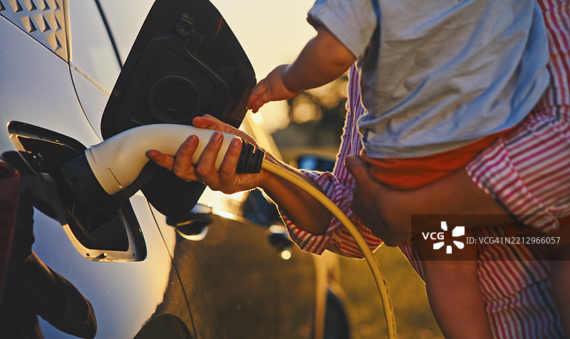 母亲在乡村里抱着小男孩插入电动车充电器图片素材