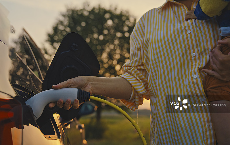 母亲在乡村环境中抱着男婴为电动车充电图片素材