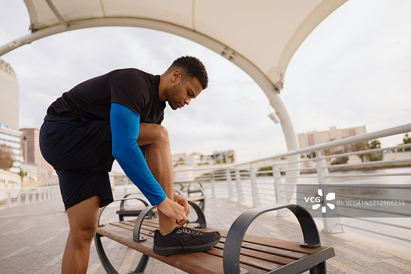 在凉棚下的长椅上系鞋带的运动男士，准备户外跑步图片素材
