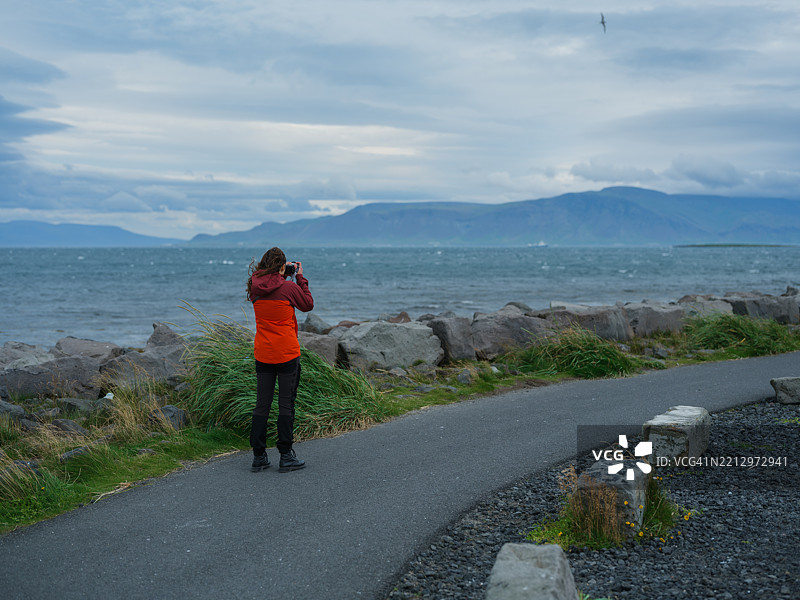 在冰岛雷克雅未克的大西洋海岸，一名女性正在用智能手机拍照。图片素材
