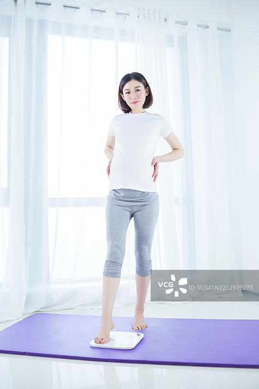 亚洲孕妇在家中站在秤上测量体重图片素材