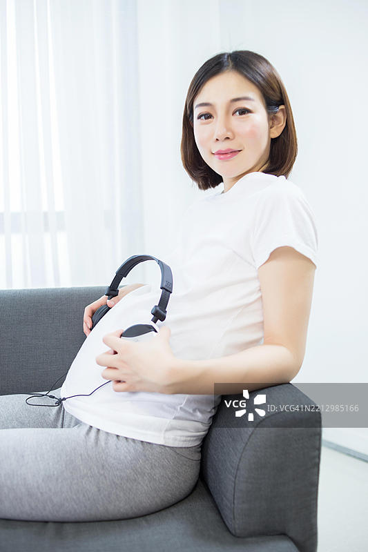 孕妇用耳机听音乐，耳机放在肚子上图片素材