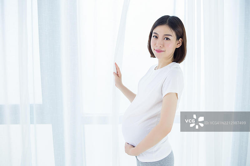 亚洲孕妇站在窗边图片素材