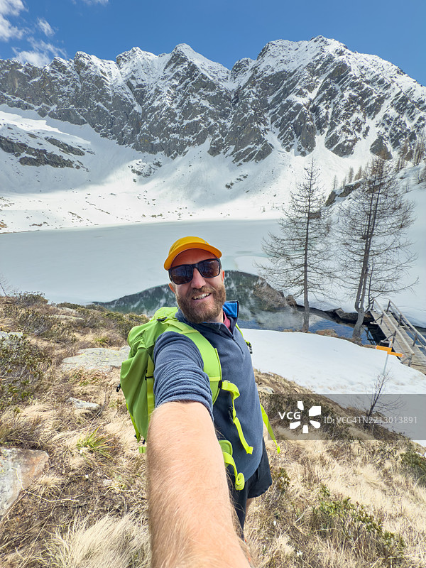 男子在被雪覆盖的山湖旁徒步旅行自拍图片素材