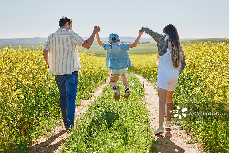 在田野中与家人牵手，背着或抱着孩子，增进感情、玩耍或冒险度假。户外，快乐的游戏，孩子与爸爸妈妈一起在大自然中散步，享受假期、爱或旅行。图片素材