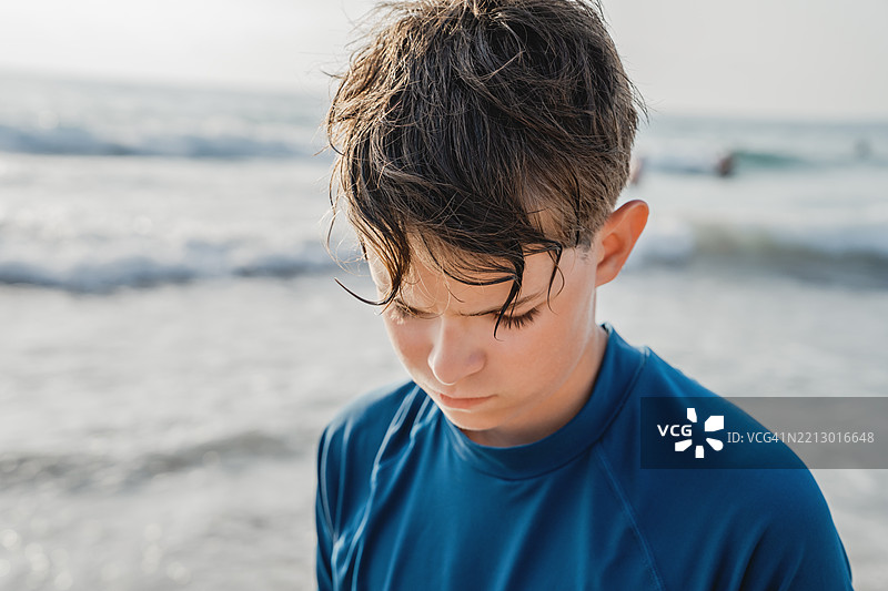 放松而困惑的少年游泳者坐在海滩上，夕阳西下。图片素材