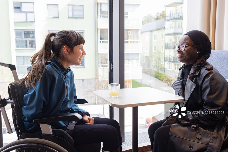 微笑的少女坐在轮椅上，与她的残疾支持工作者在咖啡馆环境中。图片素材