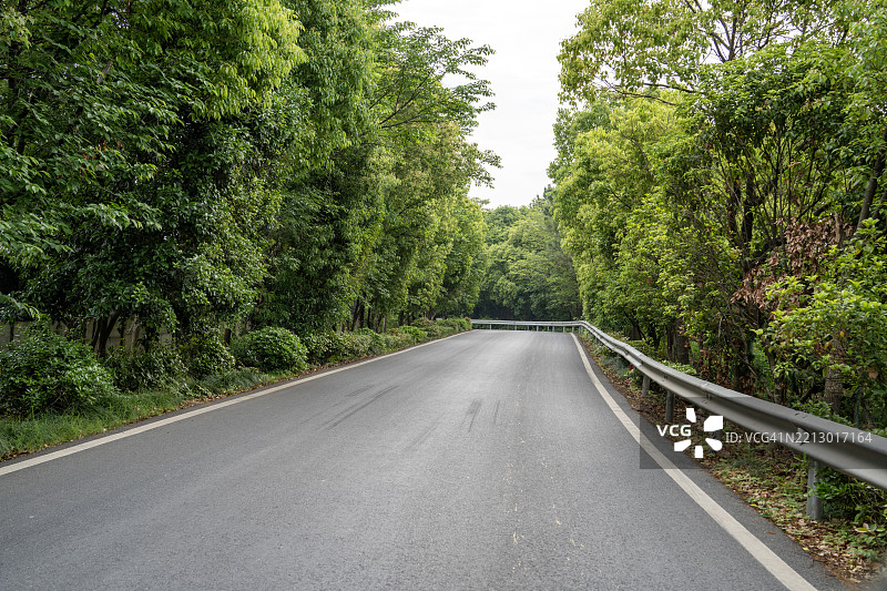 空旷的乡村道路，旁边有护栏和树木遮蔽图片素材