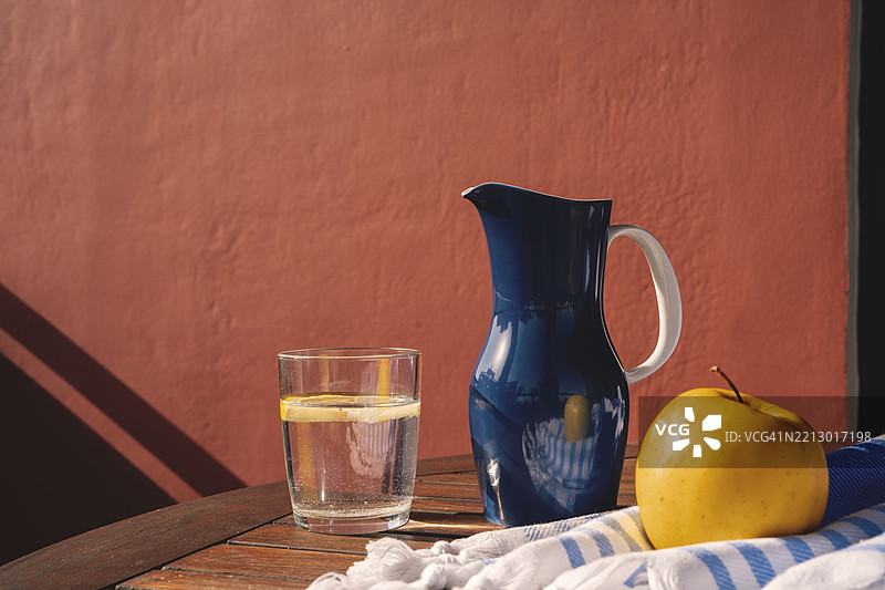 夏季露台上的桌子上放着一杯柠檬水和一个蓝色水壶图片素材