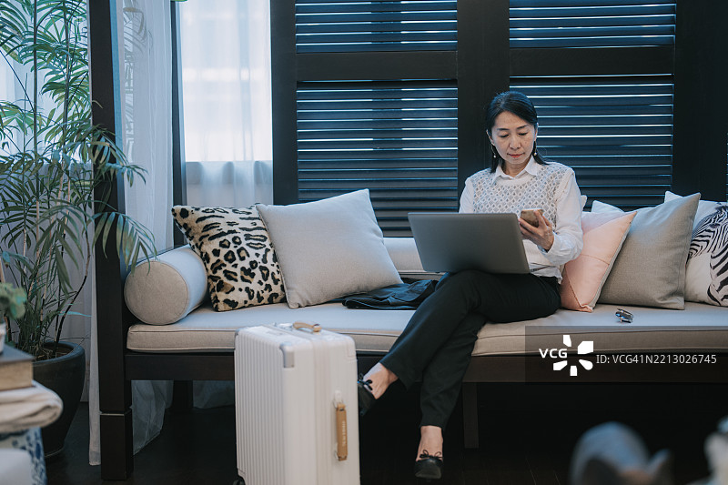 亚洲女商人在时尚休息室中远程工作，旁边有行李。图片素材