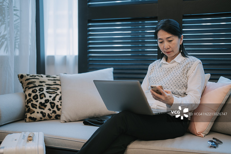 亚洲女商人在时尚休息室中远程工作，旁边有行李。图片素材