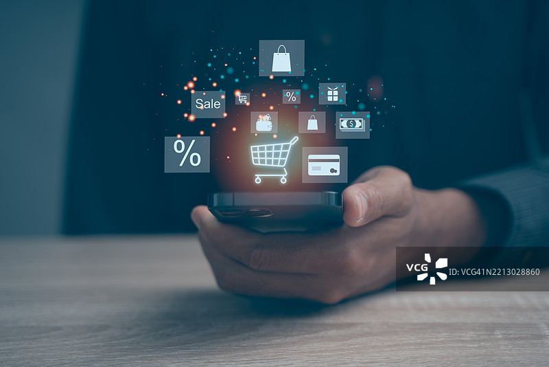 手握智能手机，屏幕上显示购物图标，背景为深色图片素材