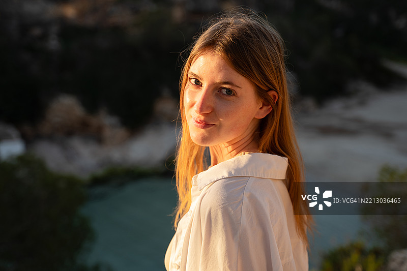 年轻女性在日落时分靠近水边回头望去图片素材