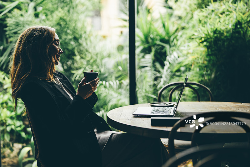 一位女性在餐厅里用笔记本电脑分析商业报告，同时喝着一杯咖啡。图片素材