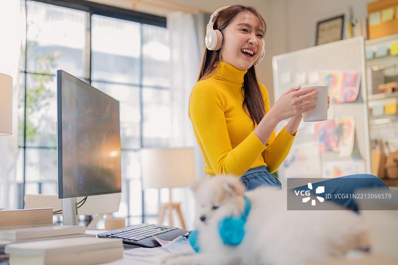 亚洲创意机构的女性穿着休闲服装，在家中工作，设计广告媒体出版，同时听着音乐，身边有她的小白色博美犬，工作室充满创意氛围。图片素材