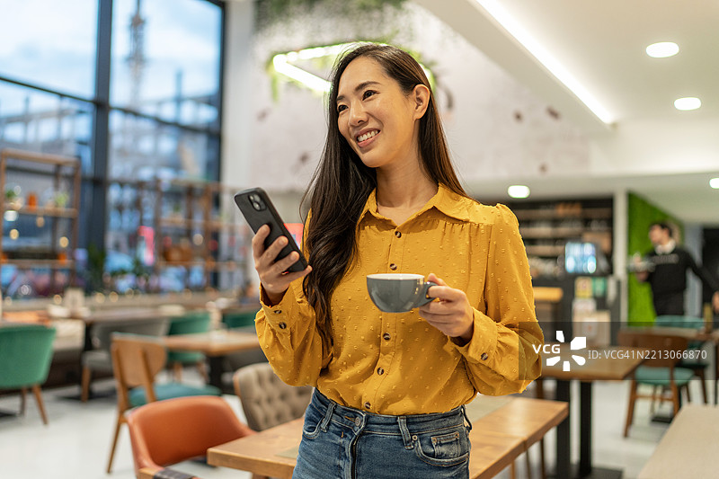 年轻的亚洲女性在咖啡馆里使用智能手机并喝咖啡图片素材