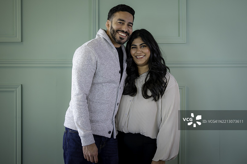 身着得体的中东印度夫妇在正式的绿色背景前的肖像图片素材