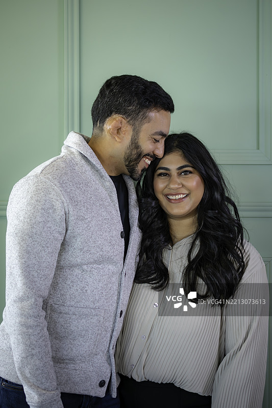 身着得体的中东印度夫妇在正式的绿色背景前的肖像图片素材