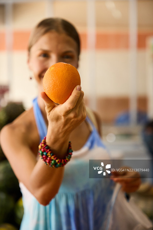微笑的女性在市场摊位展示中专注地拿着一个橙子图片素材