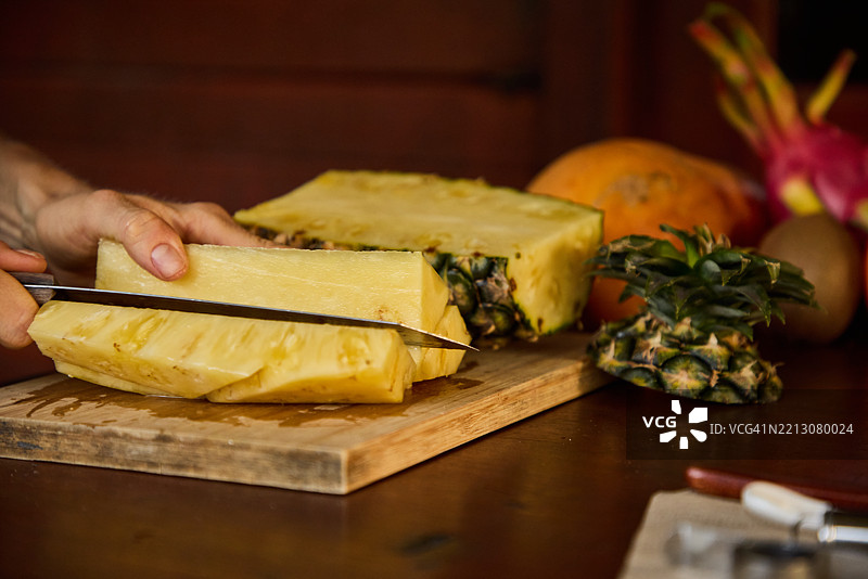 手在木砧板上切新鲜菠萝，周围摆放着热带水果图片素材